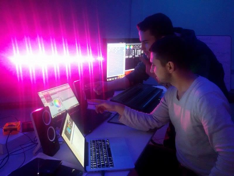 Twee mensen programmeren licht met software op een laptop; achter hen brandt roze licht